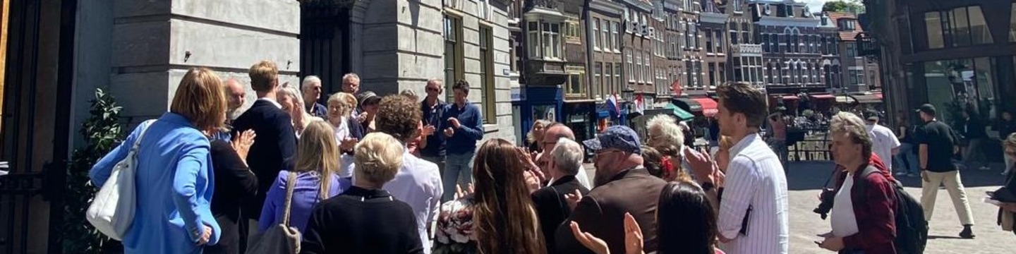 Er wordt een petitie aangeboden op de Stadhuisbrug. Er staat een grote groep mensen voor het stadhuis in Utrecht. Op de achtergrond is de Vismarkt zichtbaar.